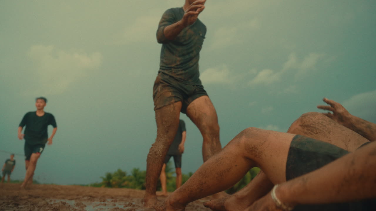 Two young men fall in muddy field during intense football in the rain, slow motion