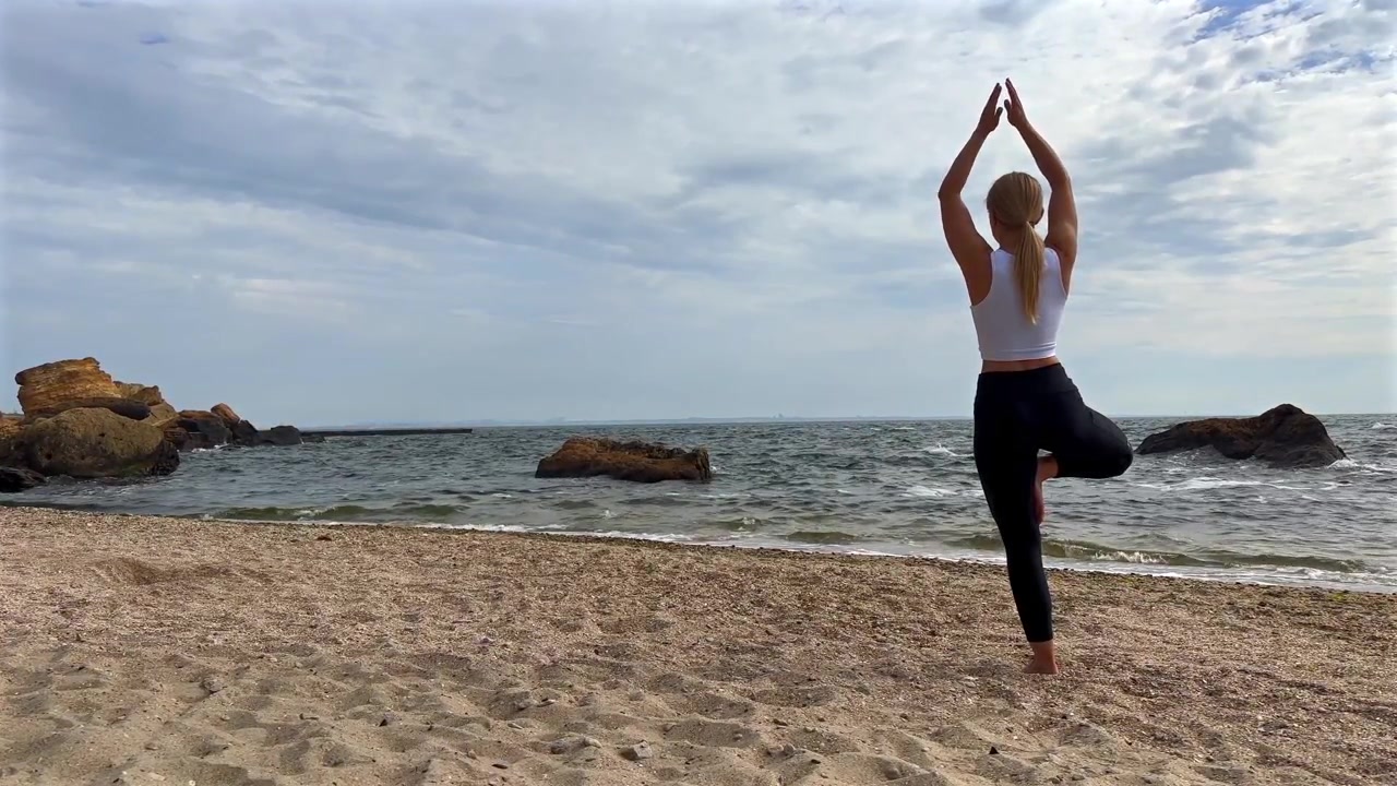 Giovane donna che pratica la posizione dell'albero yoga sulla spiaggia