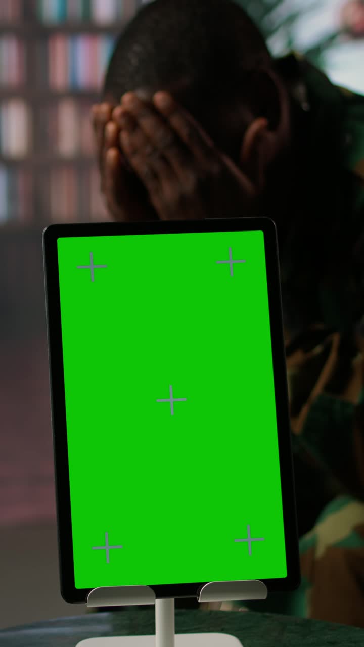 Tableta con pantalla verde y veterano angustiado de fondo