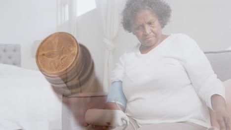 Animation-of-stack-of-coins-over-worried-senior-woman-measuring-blood-pressure-and-sitting-on-bed