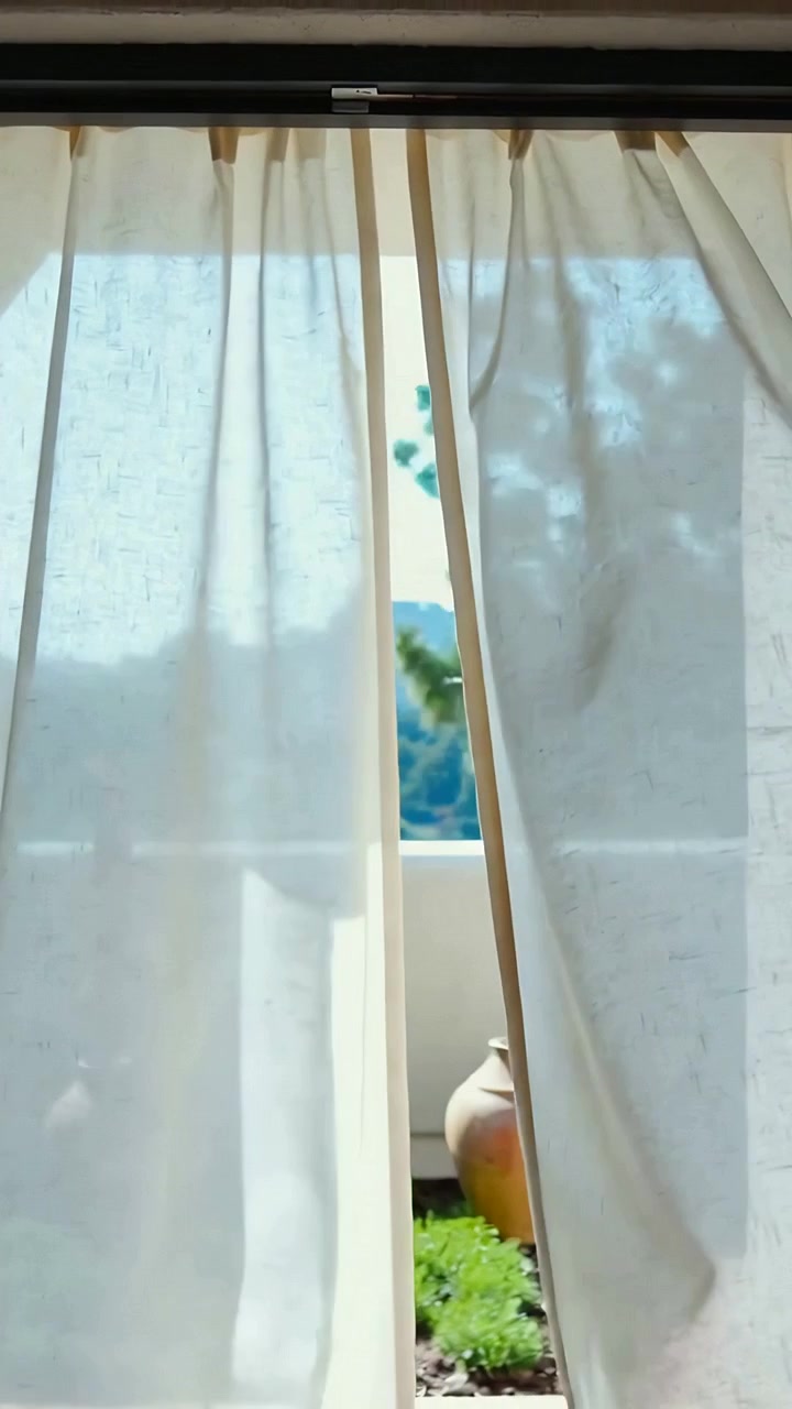 Video verticale: Un paio di tende beige ondeggianti che si muovono con la brezza, rivelando una fioriera da balcone
