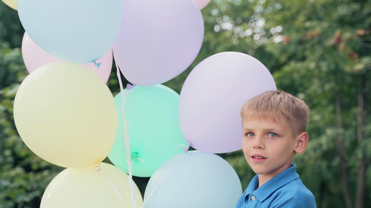 Cheerful boy is spinning with inflatable balls in his hands. Multi-colored helium balloons for the holiday. Portrait of a child in a blue shirt