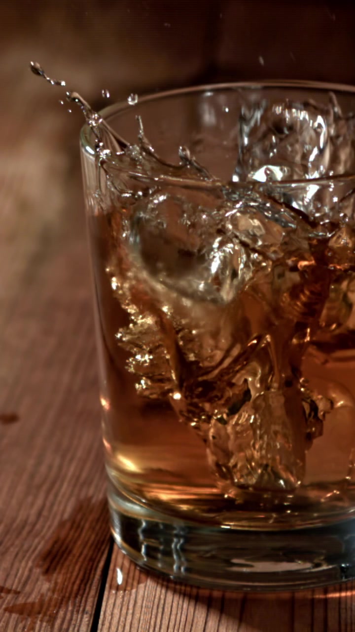 Cubetti di ghiaccio che schizzano in un bicchiere di whisky al rallentatore.