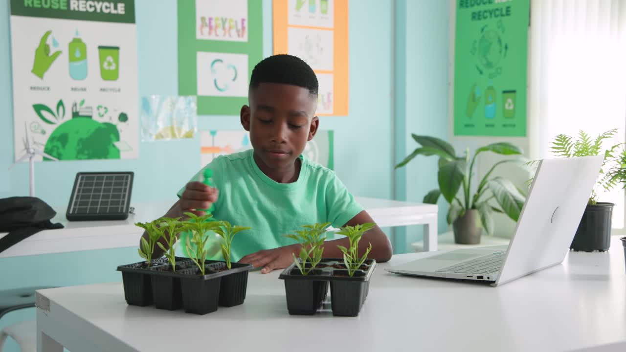 youth leaning inspecting seedling trays misting bottle checking laptop for class at school