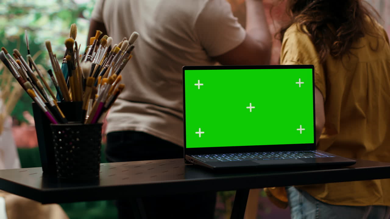 Laptop with green screen in art studio with artists and paint brushes