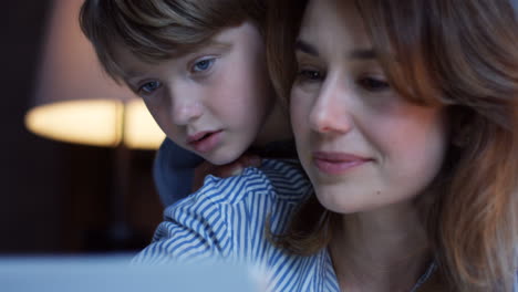 Close-up-view-of-the-charming-woman-doing-or-watching-something-on-the-tablet-while-his-small-son-looking-out-over-her-shoulder