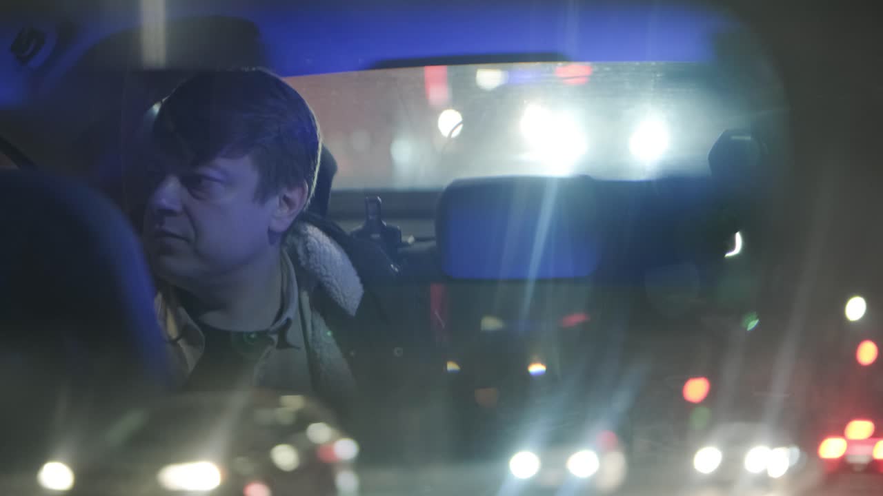 cámara lenta de primer plano de un joven hombre de negocios guapo mirando hacia afuera durante un viaje en un coche moderno con un conductor en el centro de la ciudad por la noche. luces de la ciudad