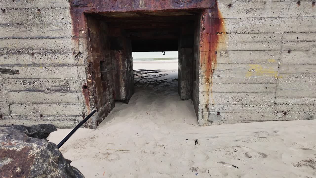 The entrance to an old, dilapidated WW2 bunker which is half filled with sand. History of Denmark.