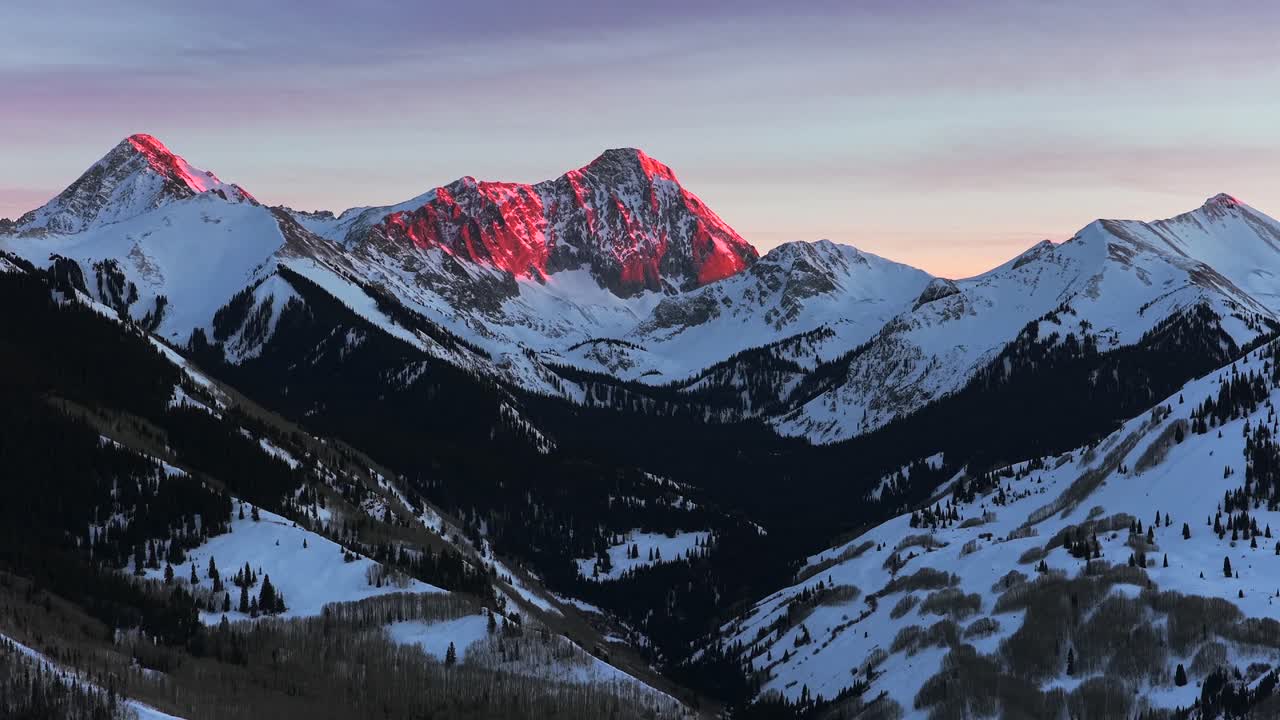 Tramonto invernale vibrante, rosso fuoco, sul paesaggio panoramico naturale del Capitol Peak Wilderness, Colorado 14er, ripreso da drone aereo sulla valle di Aspen Snowmass e la Catena montuosa Elk; le ultime luci illuminano le Montagne Rocciose, Longs Peak e Maroon Bells, in una panoramica inversa.