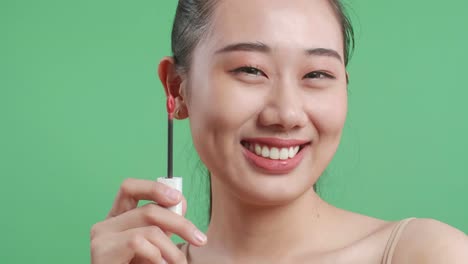 close up de una mujer asiática con lápiz labial y sonriendo a la cámara mientras está de pie en el fondo de la pantalla verde en el estudio