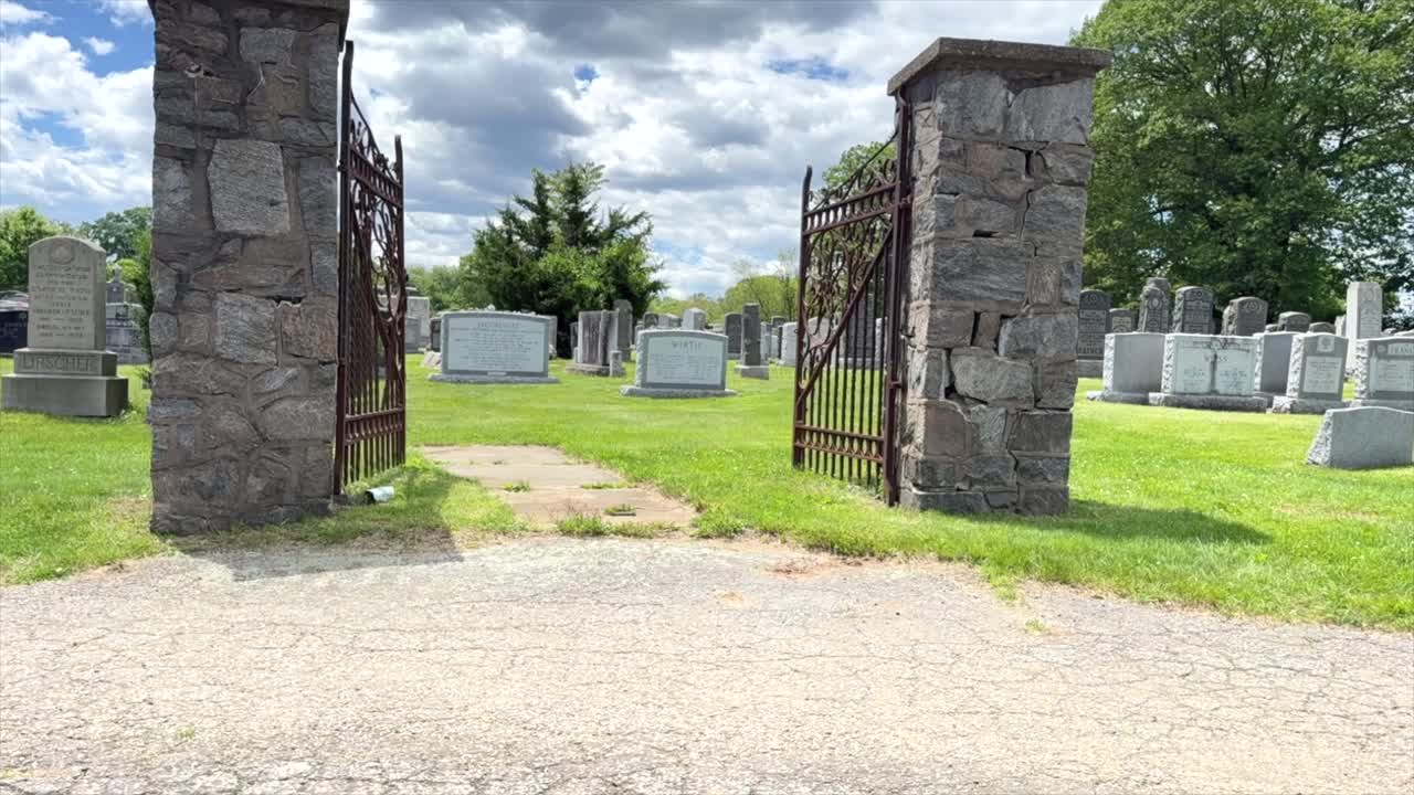 Time lapse di un cimitero ebraico con grandi lapidi che passano attraverso un cancello metallico indipendente durante il giorno mentre le nuvole si muovono.