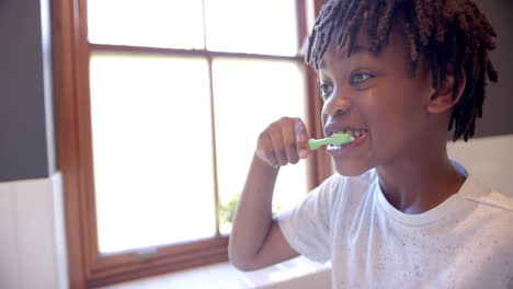 niño afroamericano cepillándose los dientes en el baño en casa, en cámara lenta
