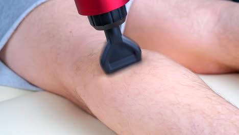 masajista que masajea los músculos de la pantorrilla de un deportista con un masajeador de percusión