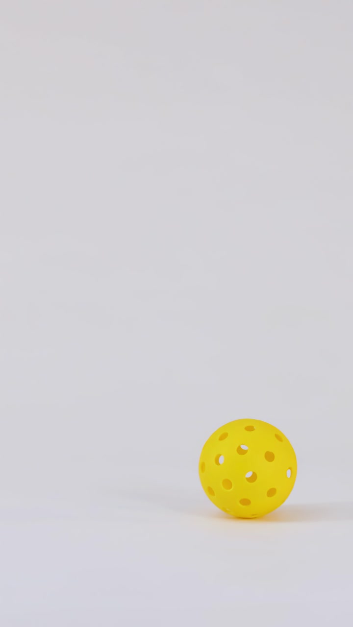 A single yellow pickleball falls vertically, bounces once, and settles on a white surface