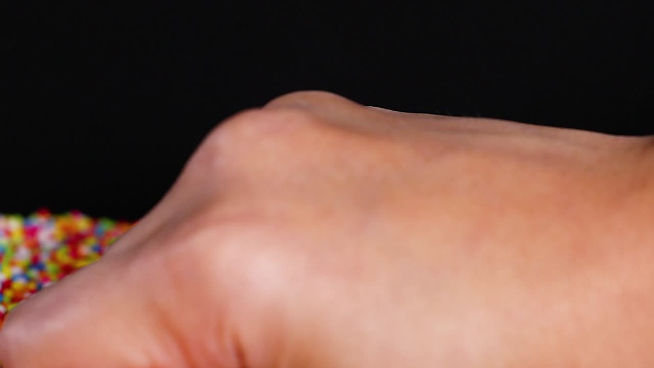 Close-up of hands interacting with falling colorful sprinkles against a dark background.