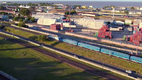 Aerial-view-dolly-in-of-a-train-with-unoccupied-rails-on-the-sides,-containers-stacked-in-a-warehouse