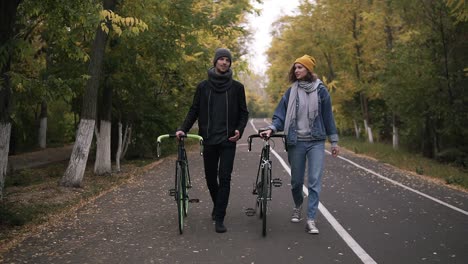 Two-Close-Friends-Having-Lovely-Talk-While-Walking-With-Bikes-In-City-Park-Between-Green-And-Yellow-Tall-Trees,-Concept-Of-Active-Lifestyle,-Communication,-Dating,-Autumn-Time