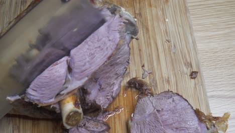 Slicing-Lamb-roast-on-the-bone-with-cleaver,-Juicy,-static-shot
