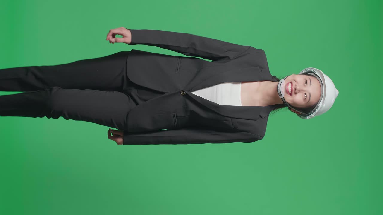 Smiling Asian Female Engineer Looking Around And Shaking Her Head While Walking In The Green Screen Studio