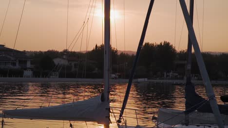 sailboats masts backlit by the setting sun, golden sunset on lake garda, italy
