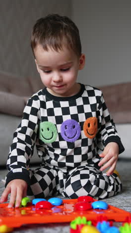 kid in black and white checkered pajama sits on the carpet. toddler plays with toy constructor. vertical video.