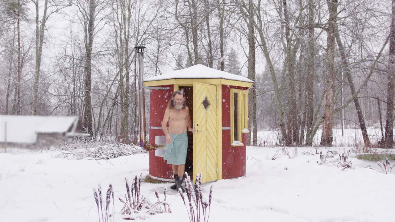 Scruffy bare chested man exit hot wooden sauna into white snowy winter landscape