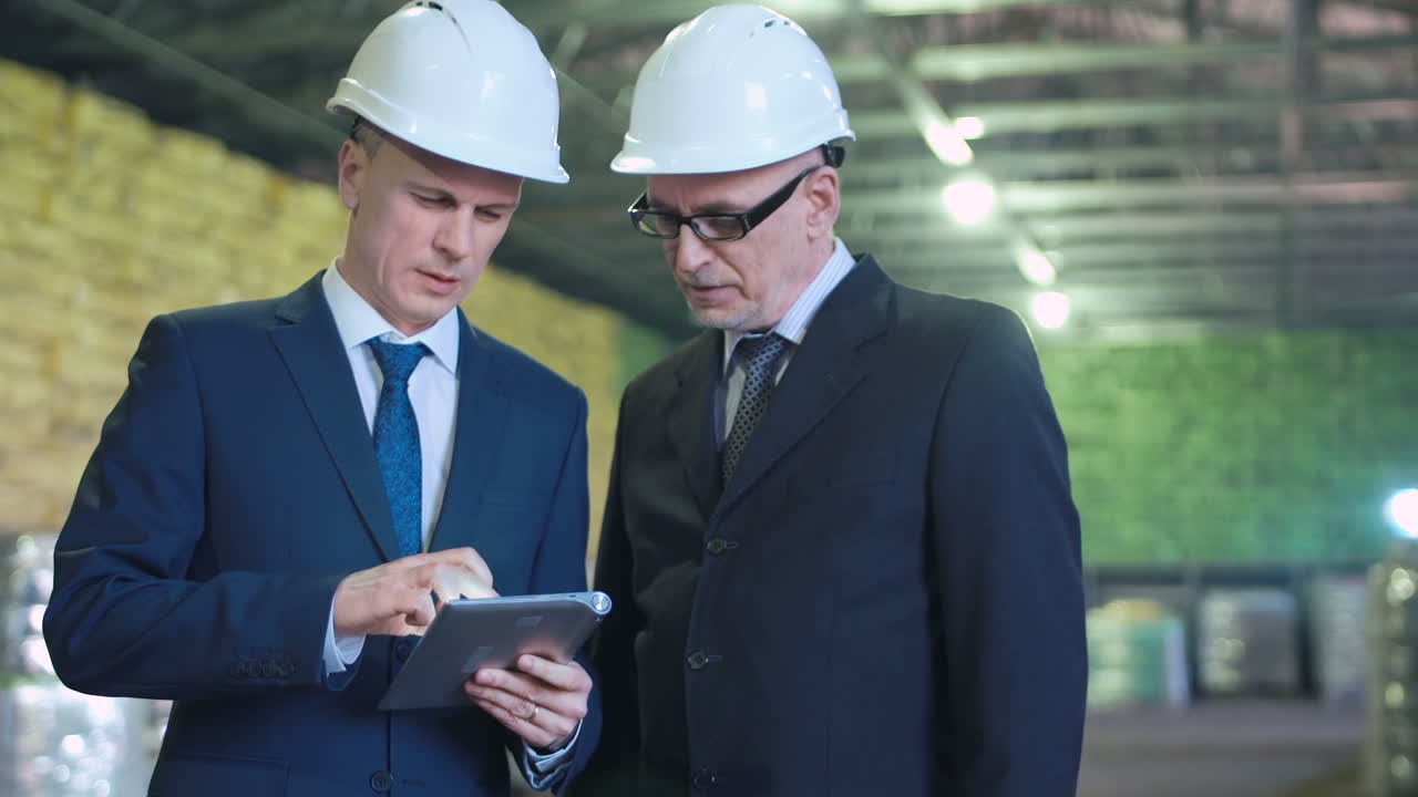Engineers or Managers Reviewing Plans on a Tablet in a Warehouse