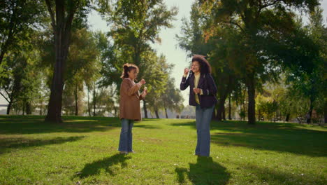 Madre-Relajante-Soplando-Pompas-De-Jabón-Con-Una-Linda-Hija-En-Un-Día-Soleado-En-El-Parque.