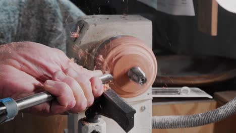 hombre viejo usando un torno y un cincel para cortar madera y liberar un grommet de metal