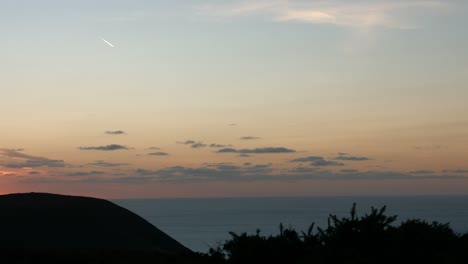 Amazing-Sunset-Golden-Hour-Footage-of-Sun-Setting-Behind-Coastal-Mountain-with-Clouds-and-Plane-Contrails-Devon-UK-4K