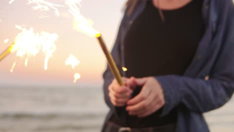 Group-of-friends-holding-sparkling-candles-and-lightning-them-up-on-the-beach-during-sunset