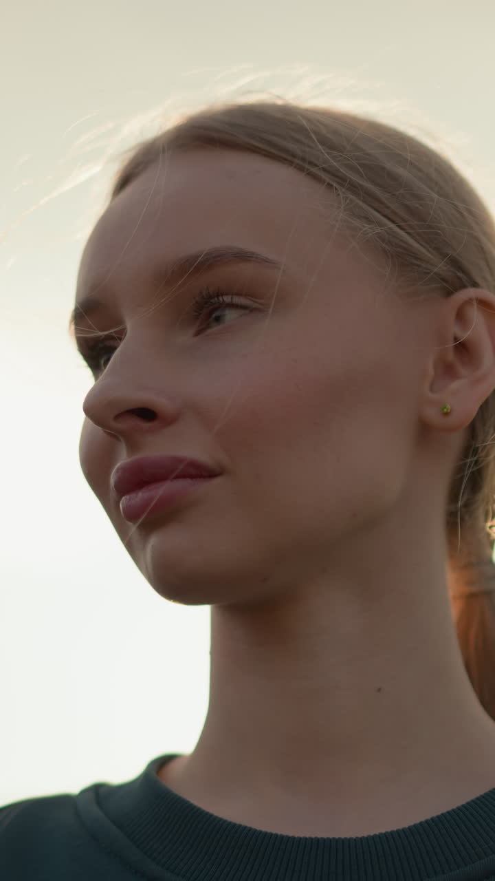 una dama con una camiseta verde con labios rosados mira pensativamente hacia el horizonte bajo un cielo brillante, capturada en un momento pacífico de contemplación, con la luz del sol brillando a su alrededor