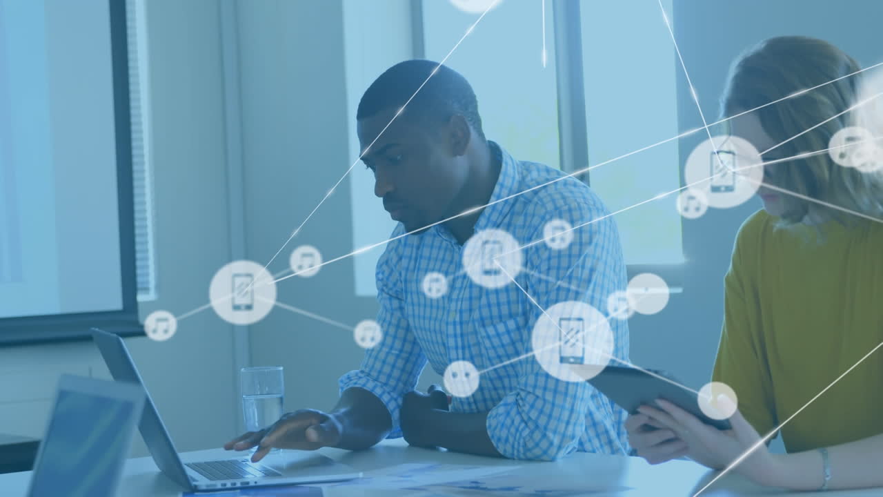 Animation of connected icons over diverse coworkers working on laptop and digital tablet in office