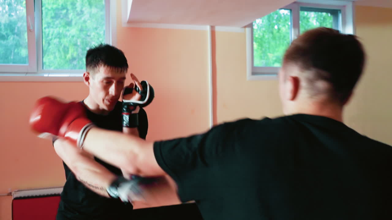 Fighters engaged in intense sparring inside gym, one throwing powerful punch while opponent ducks, both wearing gloves and black shirts, showcasing speed, strength, discipline, combat training