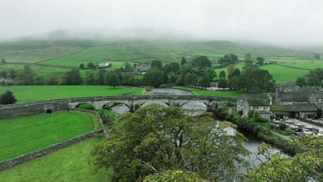 Slowly-tracking-forwards-and-up-over-trees-towards-bridge-in-overcast,-Yorkshire,-United-Kingdom