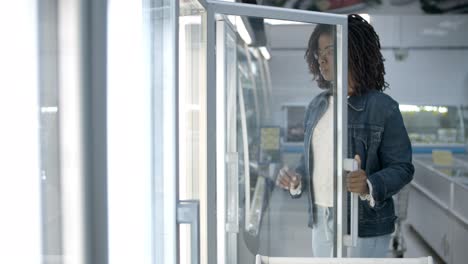 Focused young woman choosing goods from fridge