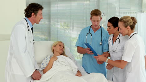 Medical-team-looking-at-clipboard-and-speaking-together-with-patient