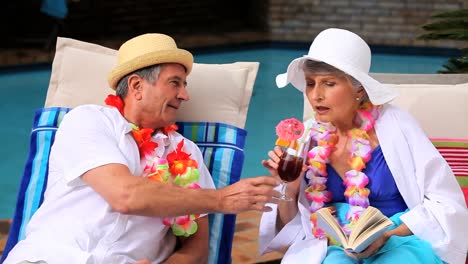 mature couple enjoying their cocktails by the pool