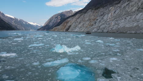 Drone-view-of-floating-melting-icebergs-and-tour-boat-sailing-in-Endicott-Arm-Fjord,-Inside-Passage,-Alaska