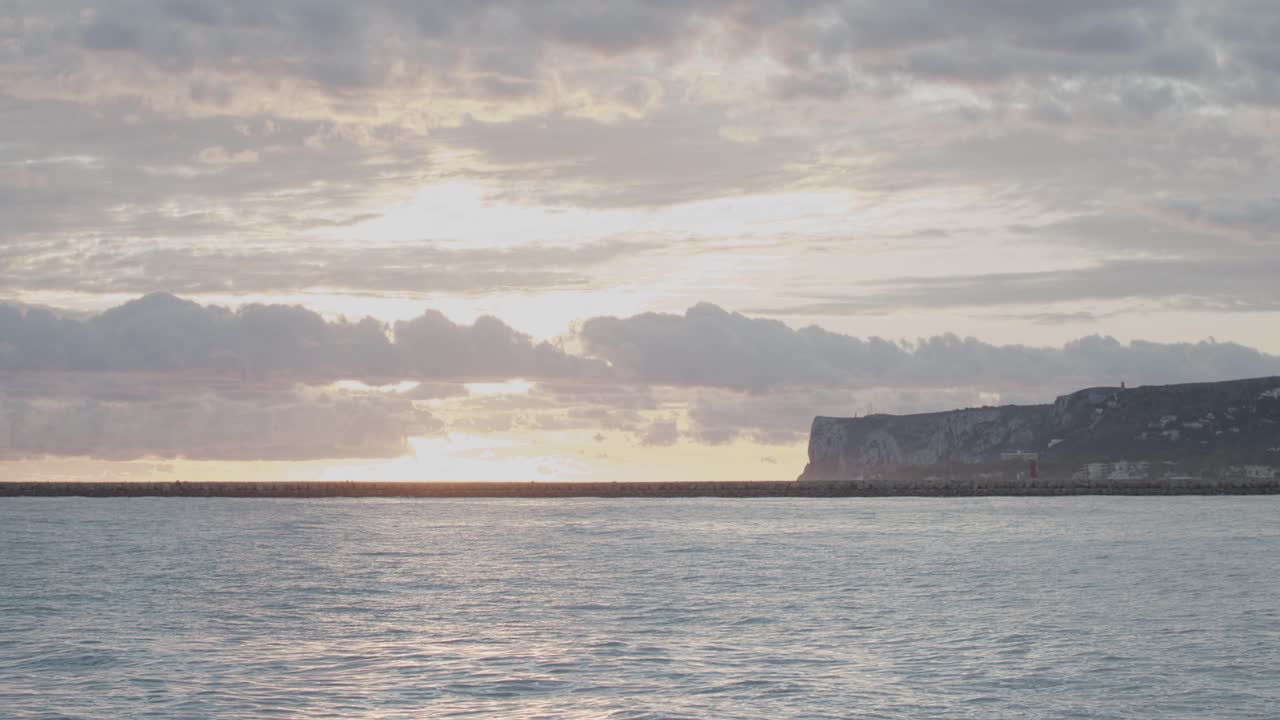 timelapse de 4k del sol saliendo detrás de las nubes en el mar mediterráneo con la montaña al fondo