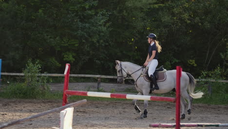 professional girl rider galloping on a horse. girl riding a horse on an arena at sunset. horse hoof creates a lot of dust. competitive rider training jumping.