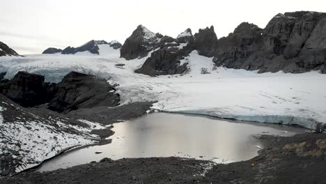 Sobrevuelo-Aéreo-Desde-Las-Orillas-Hasta-El-Lago-Glacial-Del-Glaciar-Claridenfirn-En-Uri,-Suiza-Al-Atardecer-Con-Una-Vista-Del-Cielo-Brillante-Detrás-De-Los-Picos-Alpinos-Y-Los-Icebergs-Flotantes-En-El-Agua