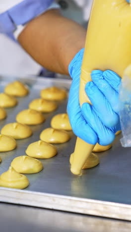 confectioner squeezes choux pastry from a bag onto the baking sheet. dough being prepared for baking in oven. close up. vertical video