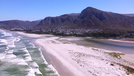 Aerial-view-of-sandbank-beach-between-estuary-and-ocean-with-mountains-in-back