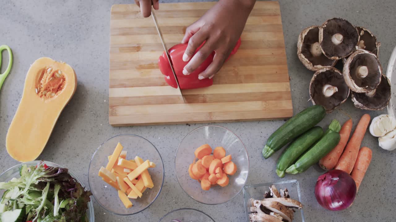 vista aérea de las manos de una mujer afroamericana cortando verduras en la cocina, cámara lenta
