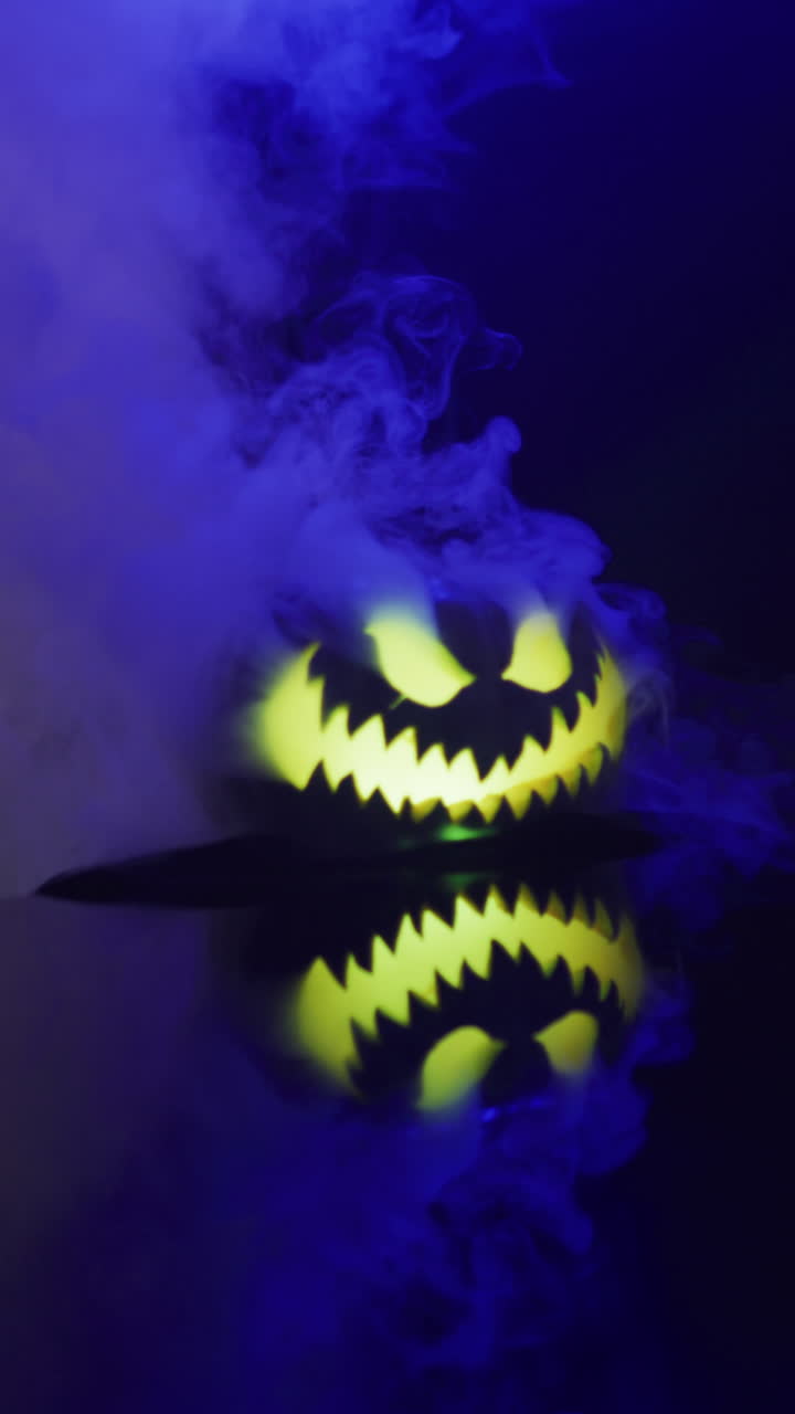 video vertical de calabaza tallada de halloween con humo y luz azul sobre fondo negro
