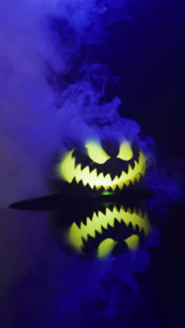 vertical video of halloween carved pumpkin with smoke and blue light on black background