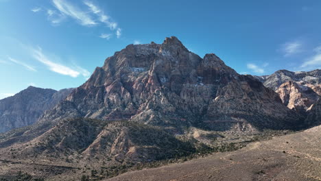 backwards tracking aerial view of lightly snow capped mountains and bright blue skies near red rock canyon in las vegas, nevada