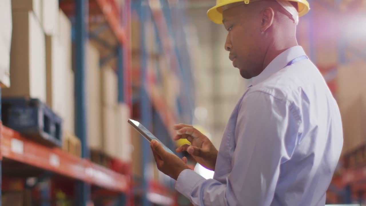 African american male worker with helmet using smartphone in warehouse