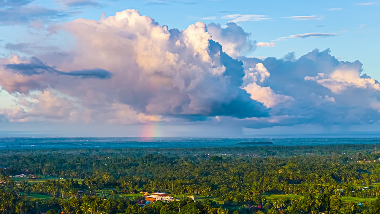 Cloud formation timelapse with rainbow in sky over Bali rural tropical landscape at sunrise, Green fields, Aerial view